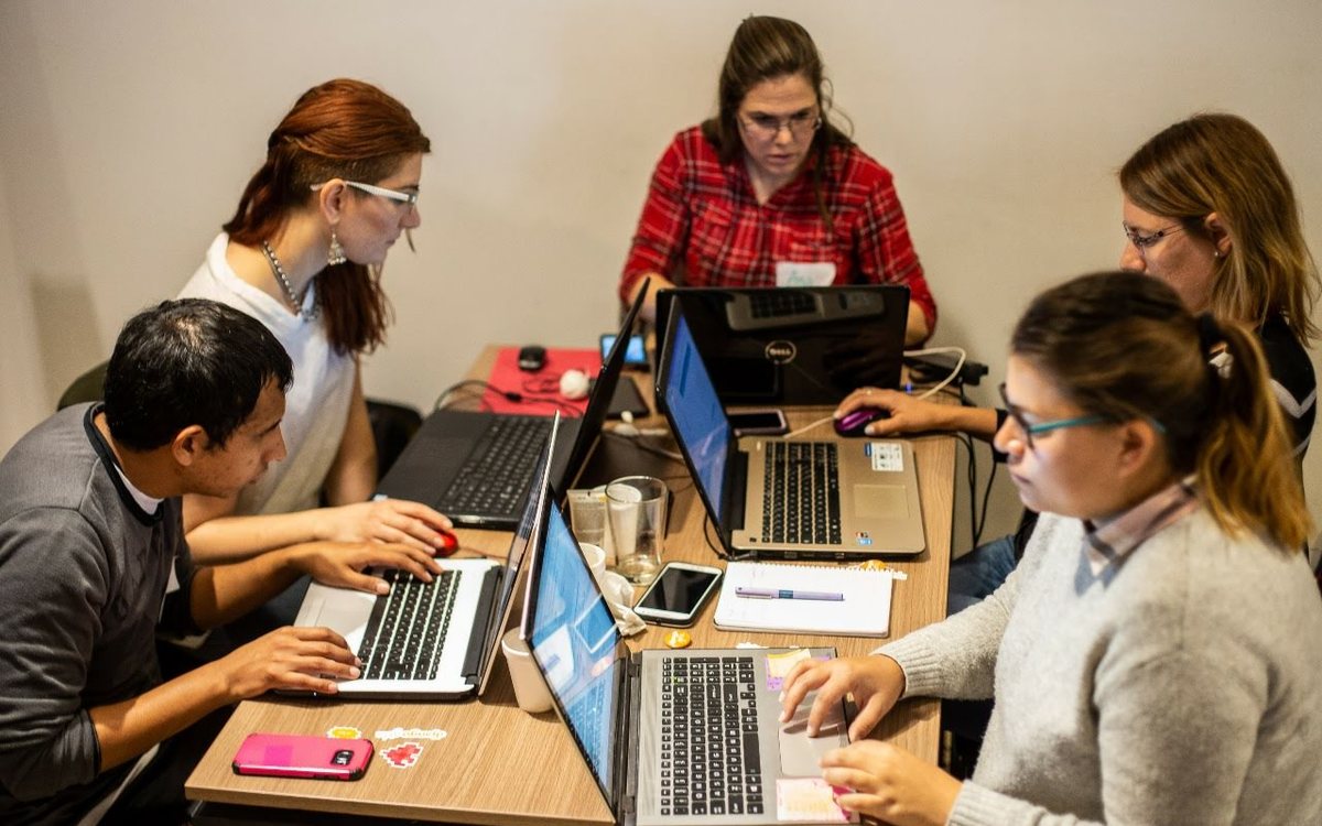 Cinco personas trabajando con sus computadoras alrededor de una mesa