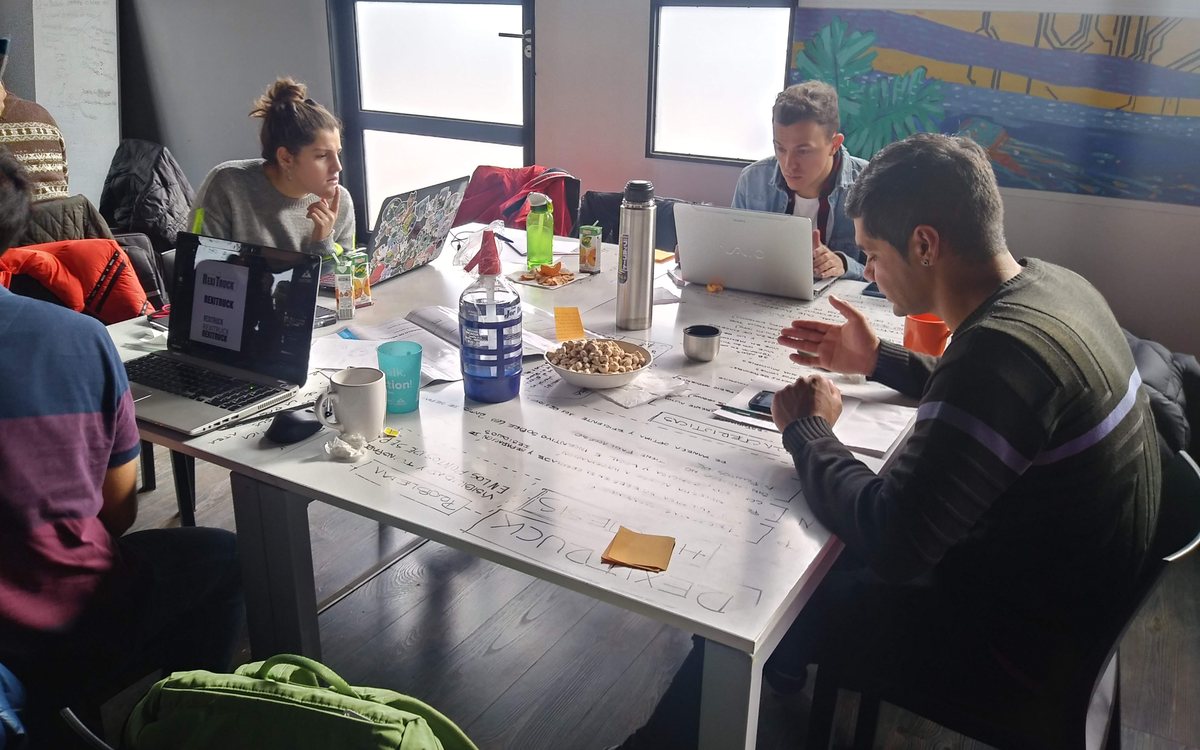 Equipo alrededor de una mesa cubierta de papel escrito, con computadoras y mate